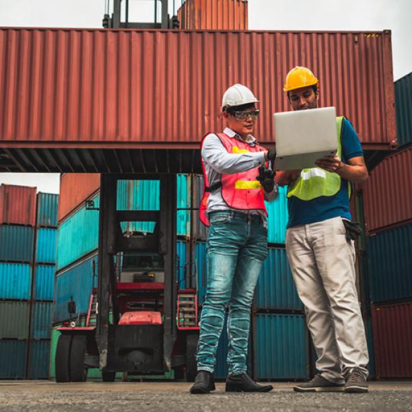 Workers looking at a laptop surrounded by containers