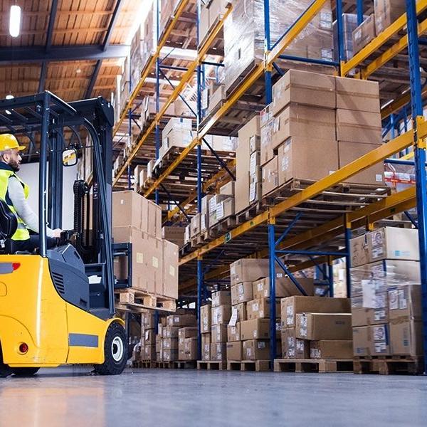 man in forklift in warehouse with racks filled with boxes